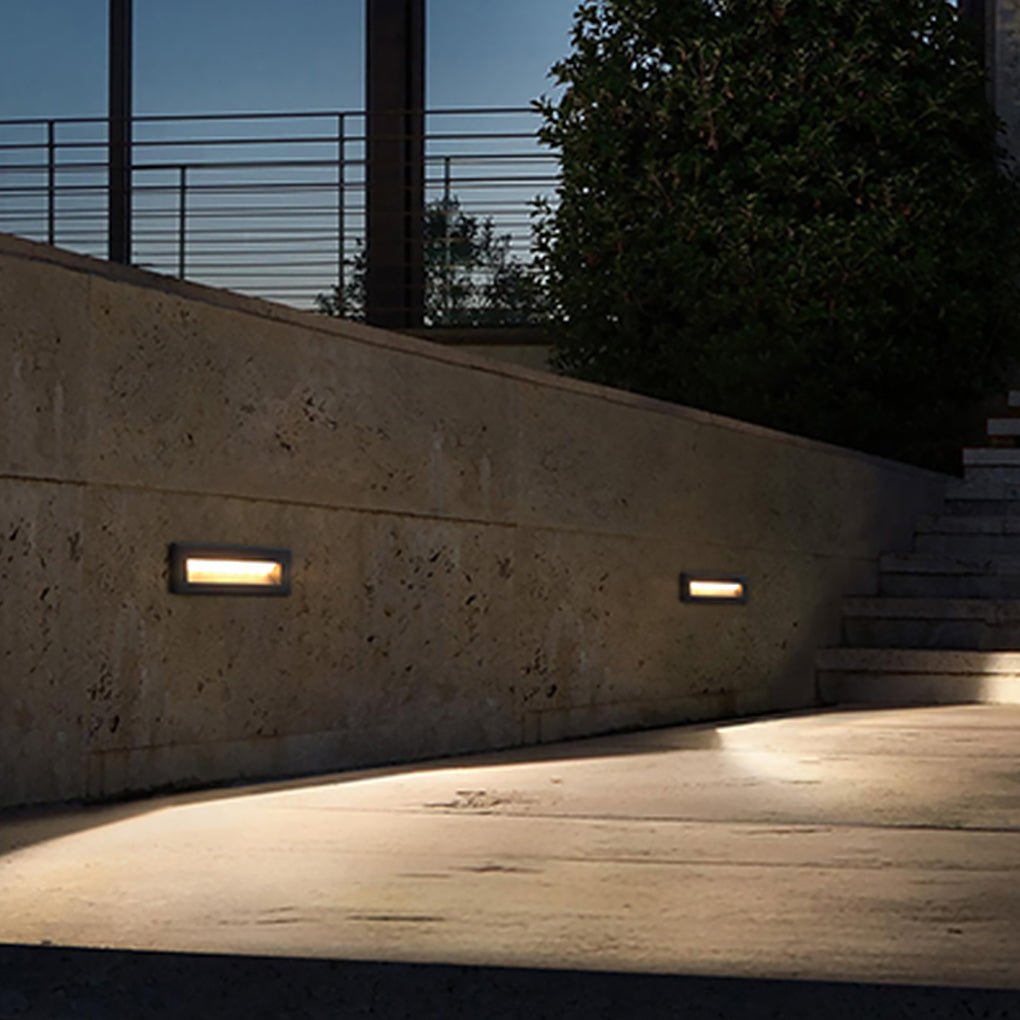 Two recessed step lights on a stone courtyard wall lighting a paved aisle