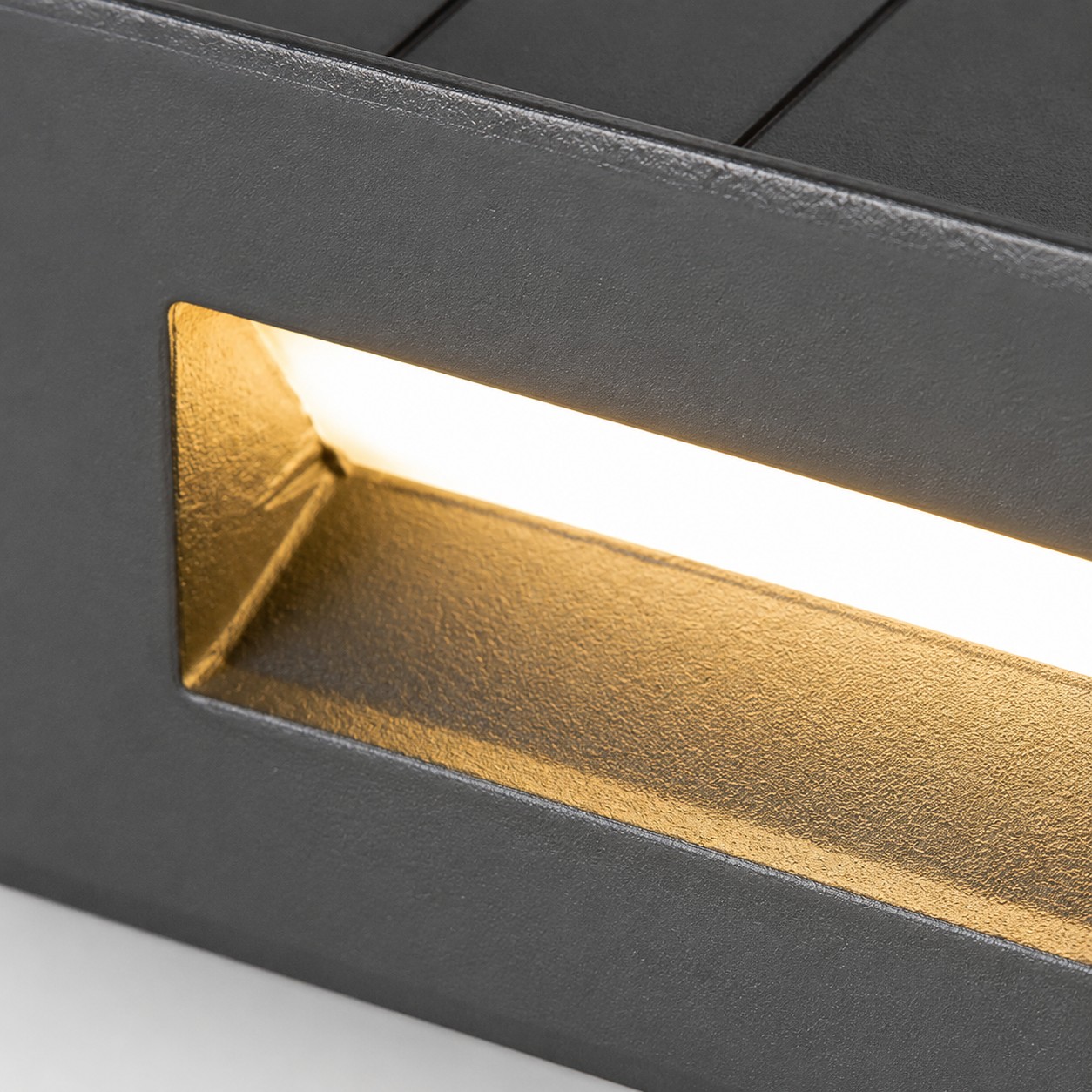 Three-quarter close-up of black recessed step light with warm downward glow from the cutout